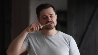 Tişörtlü adam dişlerini fırçalıyor.