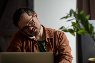 Evden bilgisayar başında çalışan bir adam telefonla arıyor.