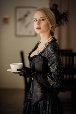 Kaliteli siyah elbiseli güzel bir kadın, elinde bir fincan çay tutuyor.
