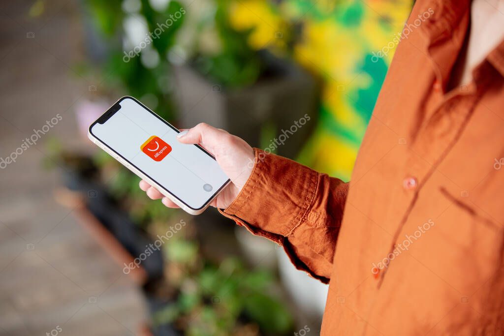 Wroclaw, Poland - 20 March 2021: woman holding iPhone 12 with China online store AliExpress logo on the screen at home