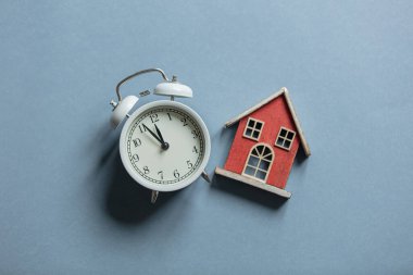 Gri arka planda klasik çalar saat ve oyuncak ev