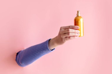 Pembe arka planda kadın el yapımı parfüm şişesi.