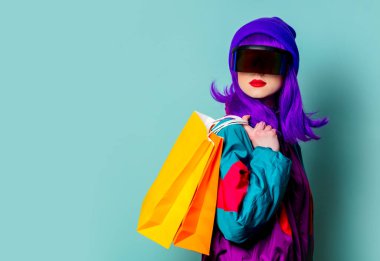 Siber punk gözlüklü şık bir kız ve 80 'lerin eşofmanı mavi arka planda alışveriş torbaları tutuyor.