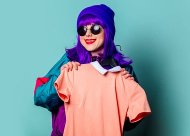 80 'ler eşofmanlı şık beyaz kız mavi arka planda elbise askısı tutuyor.