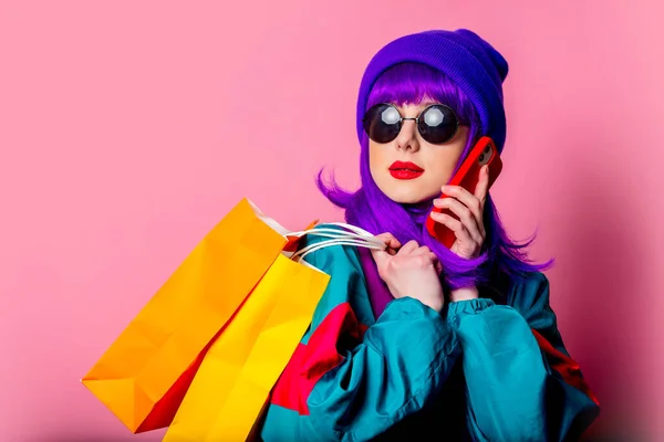 80年代のスタイリッシュなお店の女の子トラックスーツとサングラスはピンクの背景にショッピングバッグや携帯電話を保持しています — ストック写真