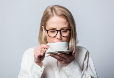 Beyaz gömlekli, beyaz arka planda kahve fincanı olan güzel sarışın portresi.