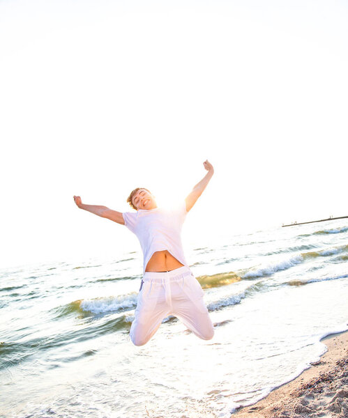 Young guy is jumping on the beach at sunrise