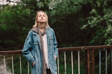 Sarışın, az ceketli, nehir kıyısında bir köprüde.