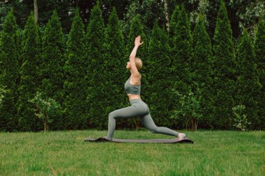 Bahçedeki çimlerin üzerinde yoga yapan genç bir kadın.