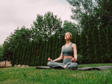Bahçedeki çimlerin üzerinde yoga yapan genç bir kadın.