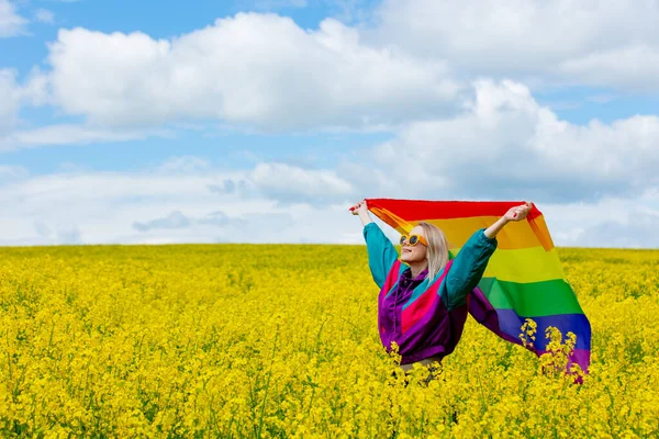 春の黄色い菜の花畑にLgbtの虹の旗を持つ女性 — ストック写真