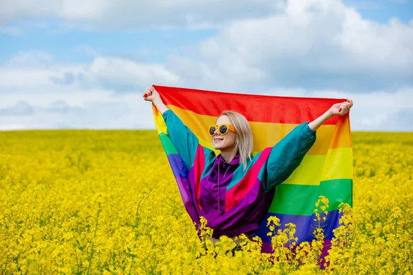 春の黄色い菜の花畑にLgbtの虹の旗を持つ女性 — ストック写真