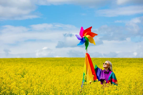 春の黄色い菜の花畑にLgbtの虹の旗とピンクホイールを持つ女性 — ストック写真