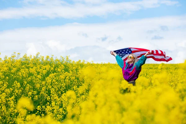 黄色の菜の花畑にアメリカ国旗を持つ女性 — ストック写真