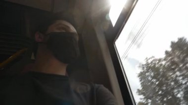 Yüz maskeli bir adam tren vagonunda oturuyor ve pencereye bakıyor.