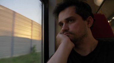 Yüz maskeli bir adam tren vagonunda oturuyor ve pencereye bakıyor.