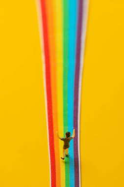 Sarı arka planda gökkuşağı LGBT şeridi üzerinde duran küçük çocuk figürü