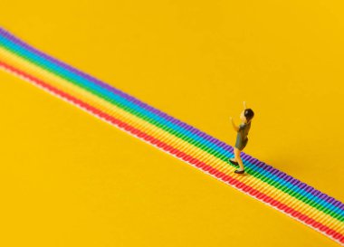 Sarı arka planda gökkuşağı LGBT şeridi üzerinde duran küçük çocuk figürü