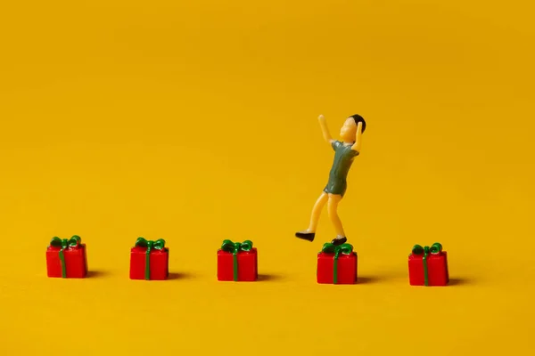 Miniaturní Chlapec Postava Skákání Červené Vánoční Dárkové Krabice Žlutém Pozadí — Stock fotografie