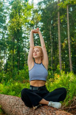 Güzel sarı saçlı kadın ormanda kütüğe oturur.