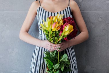 Female holding bouquet with sunset safari flowers on grey background.