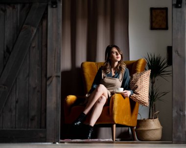 Young style woman sitting in an armchair with a cup of coffee
