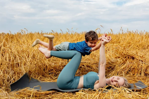 息子と母は黄金の麦畑でヨガを練習しようとします — ストック写真