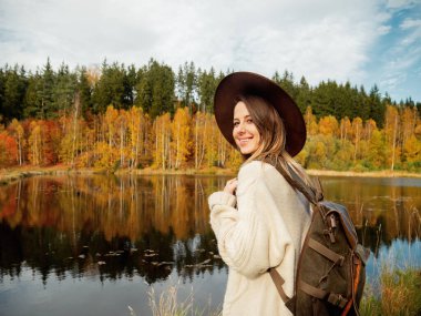 Sırt çantalı bir kadın sonbahar mevsiminde göl kenarında kalır. 