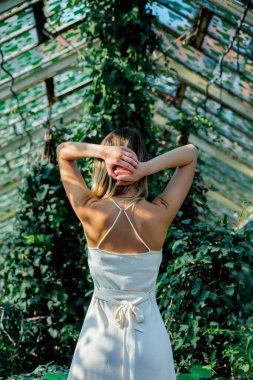 Serada sarmaşıklı beyaz elbiseli genç bir kadın.