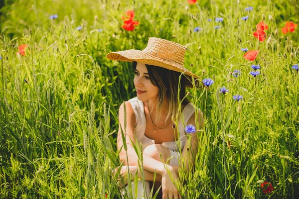 若いです女性のドレスで草の上に座ってセントーリアとポピーの花 — ストック写真