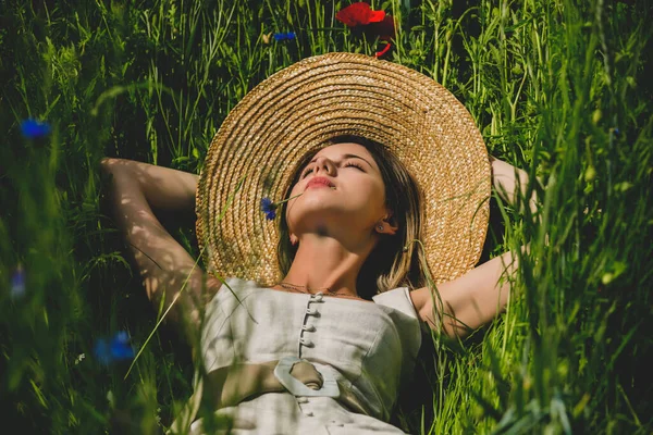 服を着た若い女性がセントーリアとポピーの花と草の上に横たわっています — ストック写真