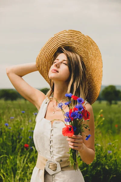 身穿连衣裙 头戴帽子的年轻女子带着一束束半人马花和罂粟花呆在田边 — 图库照片
