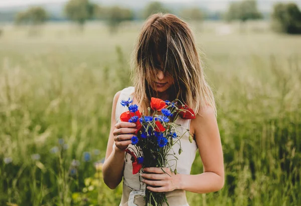 身穿连衣裙的年轻女子带着一束半人马花和罂粟花呆在田边 — 图库照片