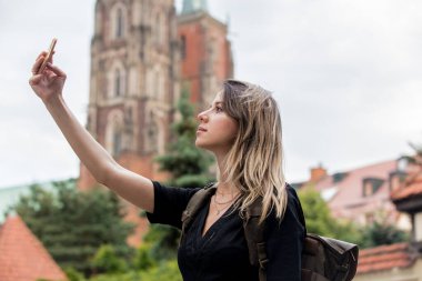 Avrupa 'daki eski kilisenin arka planında akıllı telefonu olan genç bir kız.