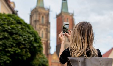 Avrupa 'daki eski kilisenin arka planında akıllı telefonu olan genç bir kız.