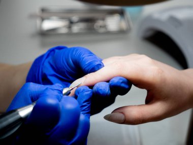 Manikür ustası çivileri makineyle temizliyor.