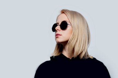 Beyaz arka planda siyah ve yuvarlak güneş gözlüklü sarışın.