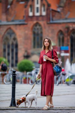 Genç bir kadın şehirde kahve içerken köpeği gezdiriyor.