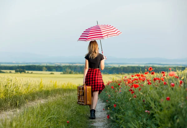 年轻女子带着雨伞和手提箱走在乡间路上 — 图库照片