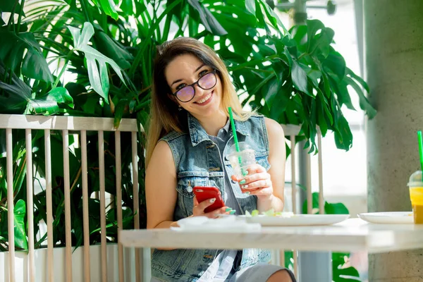 年轻女人拿着果汁 在咖啡店里用手机 — 图库照片