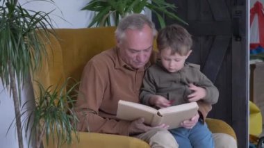 Büyükbaba torunuyla birlikte evde kitap okuyor.