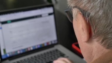 Gözlüklü yaşlı adam evde dizüstü bilgisayar kullanıyor. 4K video