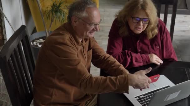 2人の高齢者が自宅のノートパソコンでサーフィンをしています 4Kビデオ — ストック動画