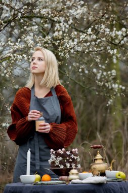 Önlüklü kadın kiraz bahçesinin yanındaki bahçede çay için masayı hazırlıyor. 