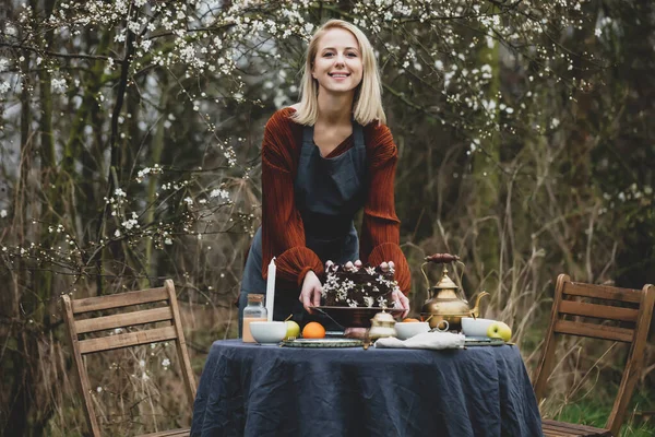 エプロンの女性はチェリーガーデンの近くの庭でお茶のテーブルを設定します — ストック写真