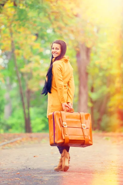 Chica morena sosteniendo maleta en el callejón de otoño en el parque — Foto de Stock