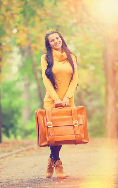 Brunette meisje houden koffer op herfst steegje in het park — Stockfoto