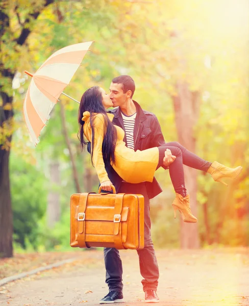 Couple with suitcase kissing at alley in the park — Stock Photo, Image