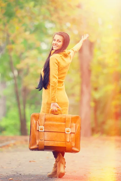 Brunette meisje houden koffer op herfst steegje in het park — Stockfoto