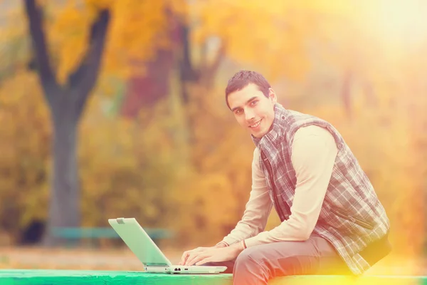 Programmeur met laptop zitten in herfst park — Stockfoto